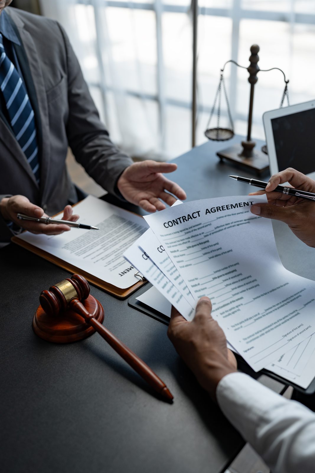 Attorneys reviewing a contract agreement at a desk with a gavel and scales of justice